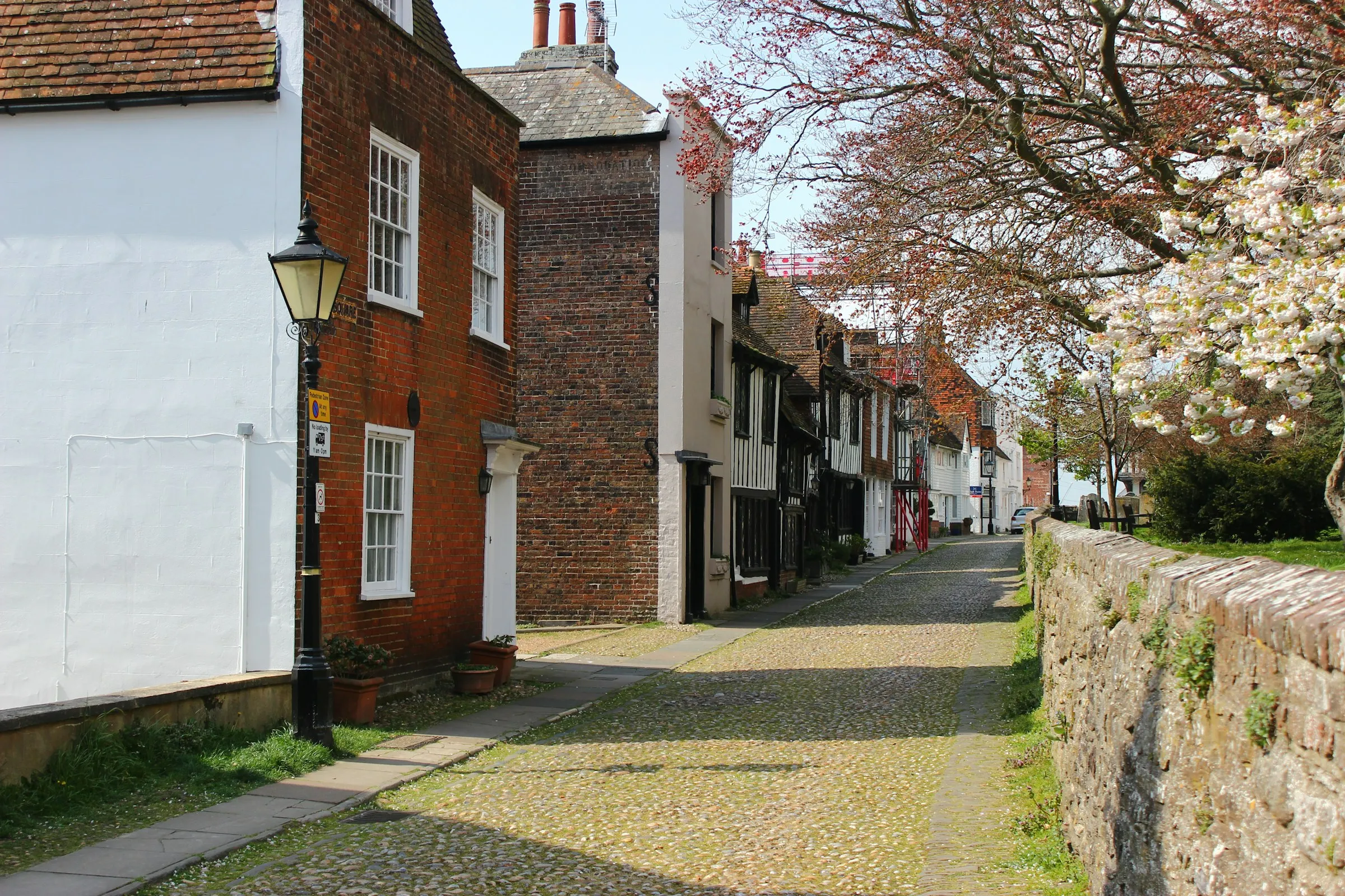 A quiet English street of brick and white-painted houses, with blossom on the trees